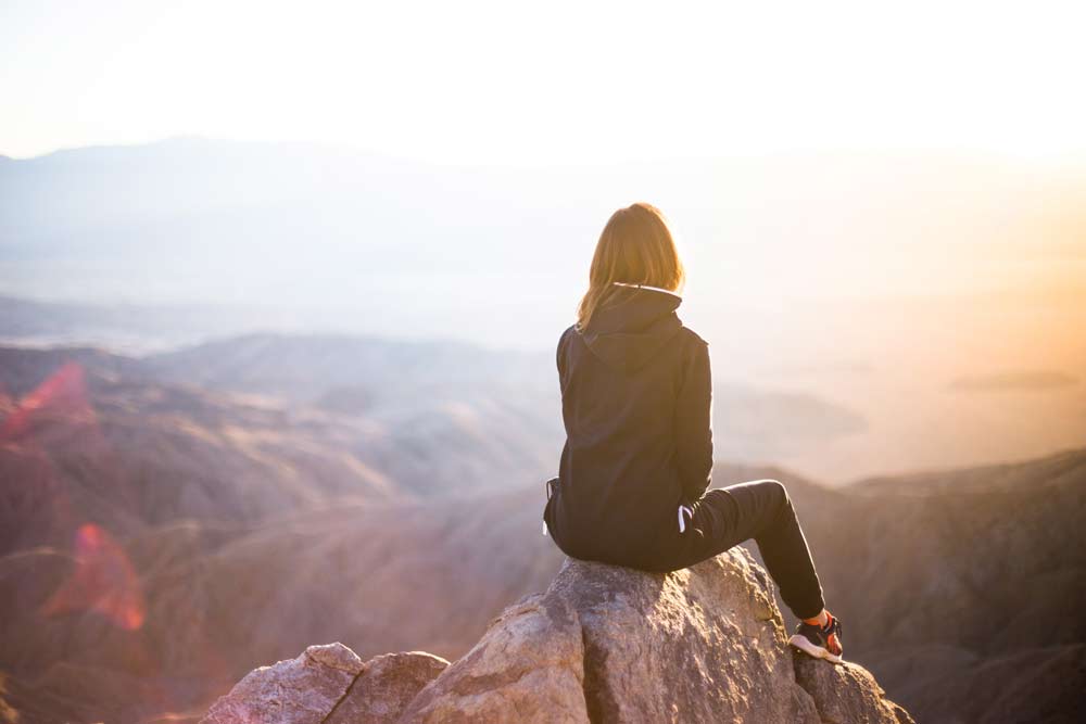 Woman sitting on top of a mountain - Financially Free